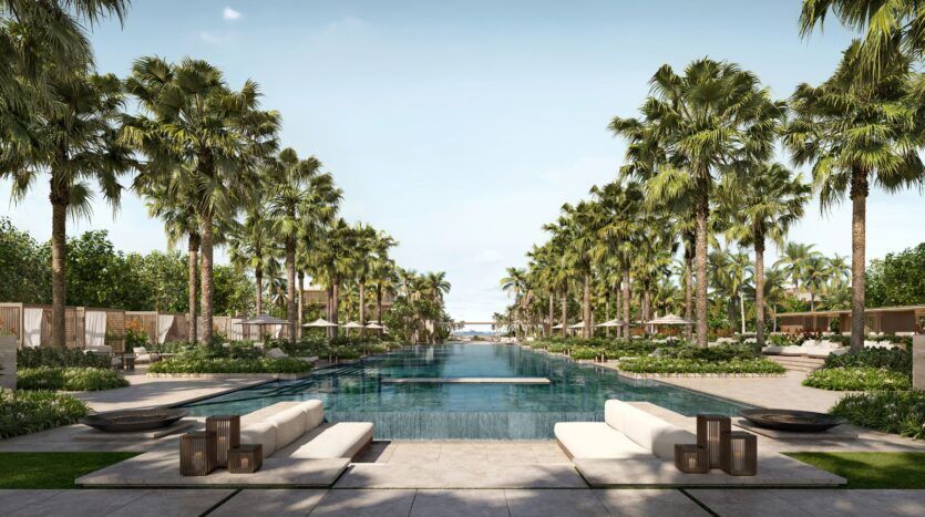 Les luxueuses résidences privées Four Seasons disposent d'une piscine extérieure bordée de palmiers et de chaises longues, menant à l'océan ; un aménagement paysager élégant et un ciel bleu clair créent une atmosphère de station balnéaire tropicale sereine.