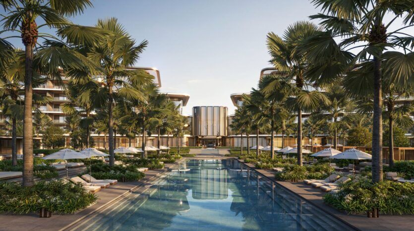 Piscine extérieure luxueuse de Four Seasons Private Residences, entourée de palmiers, de chaises longues et de parasols, avec des bâtiments modernes en arrière-plan, sous un ciel clair.