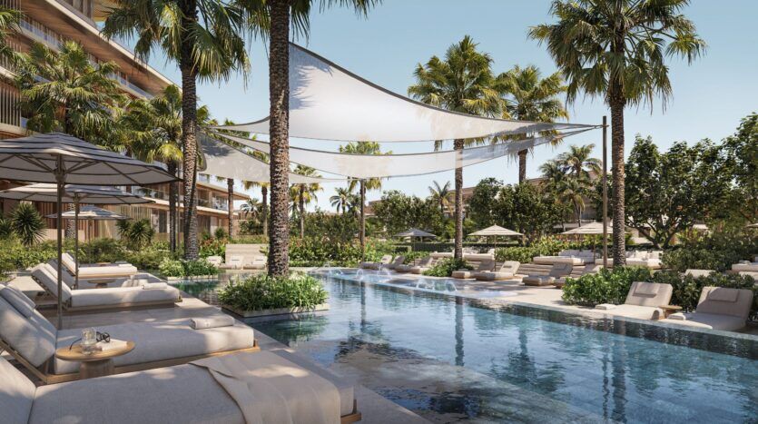 Piscine extérieure luxueuse de Four Seasons Private Residences, entourée de chaises longues, de parasols, de palmiers et d'un paysage luxuriant, avec les bâtiments modernes du complexe en arrière-plan, sous un ciel bleu limpide.