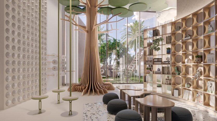 La salle de jeux moderne et aérée de Four Seasons Private Residences comprend une grande sculpture d'arbre en bois, des tables rondes et des tabourets, des étagères circulaires et de grandes fenêtres s'ouvrant sur un jardin bordé de palmiers. La décoration est légère, ludique et inspirée par la nature.