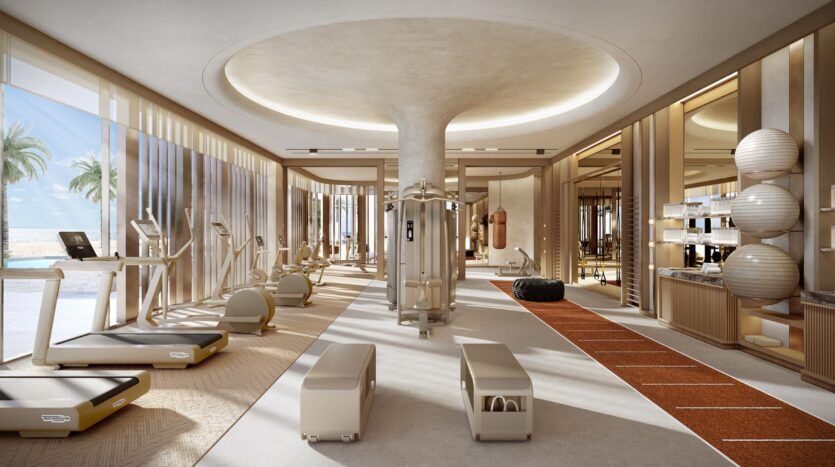 La salle de sport moderne et ensoleillée de Four Seasons Private Residences est équipée de tapis roulants, de machines d'exercice, de bancs, d'appareils de fitness, de grandes fenêtres, d'une piste de course, de murs en miroir et d'une vue sur les palmiers. L'espace se caractérise par des couleurs neutres et un design épuré.