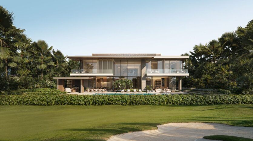 Une villa moderne de deux étages à Four Seasons Private Residences, avec de grandes baies vitrées, entourée de palmiers luxuriants et de verdure, dispose d'une piscine et d'un coin salon extérieur, donnant sur une pelouse manucurée et un bunker de sable sous un ciel dégagé.