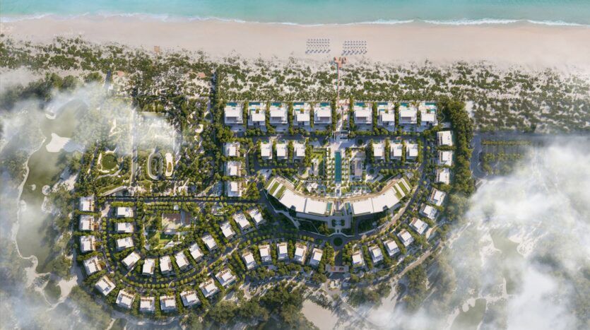 Vue aérienne du luxueux complexe hôtelier Four Seasons Private Residences en bord de mer, composé de multiples bâtiments blancs disposés en rangées courbes et droites, entourés d'une végétation luxuriante, de sentiers et d'une plage de sable fin bordant l'eau turquoise de l'océan.