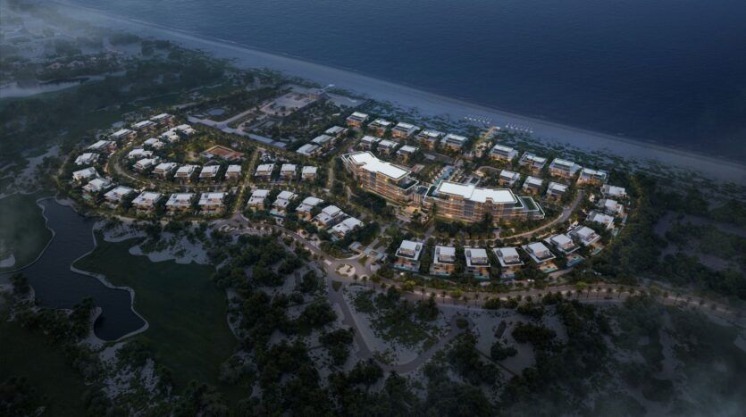 Vue aérienne nocturne de Four Seasons Private Residences, un grand complexe hôtelier en bord de mer composé de plusieurs bâtiments modernes entourés d'arbres et de verdure, situés le long d'un littoral pittoresque et reliés par des sentiers.