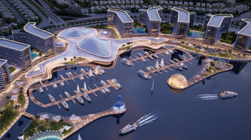 Vue aérienne d'un port de plaisance moderne avec des yachts de luxe, les bâtiments futuristes incurvés des River Cove Residences et des passerelles illuminées. Plusieurs bateaux sont amarrés et quelques-uns naviguent près de structures architecturales uniques.