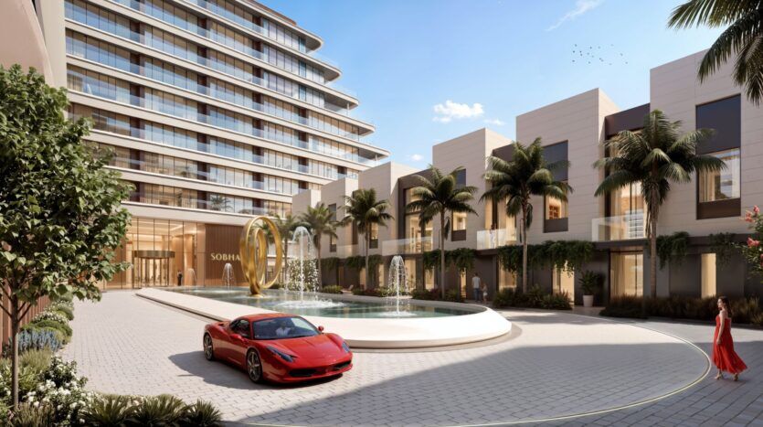L'entrée d'un hôtel de luxe moderne à River Cove Residences présente une fontaine d'eau, des palmiers, une voiture de sport rouge garée devant et une femme en robe rouge marchant à proximité sous un ciel bleu clair.