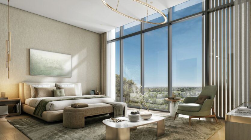 The modern, sun-filled bedroom at The Orchard by Sobha features floor-to-ceiling windows, neutral tones, a king-size bed, touches of greenery, a comfortable armchair, and a stylish coffee table, all offering a picturesque view of the outdoors.