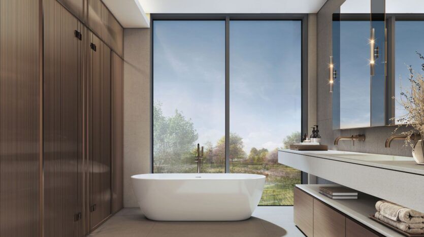 A modern bathroom at The Orchard by Sobha featuring a freestanding white bathtub, floor-to-ceiling windows, built-in wooden cabinets, a double sink with a mirror, and soft natural light flooding the space.