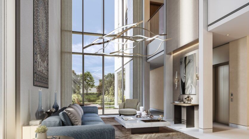 The modern, airy living room at The Orchard by Sobha features floor-to-ceiling windows, neutral tones, a blue sofa, an abstract chandelier, a marble coffee table, wall art, and a large tapestry, all overlooking a lush garden with trees and greenery.