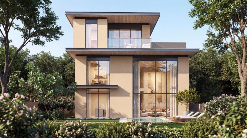 A modern three-story home in The Orchard by Sobha, featuring large floor-to-ceiling windows, a beige exterior, and spacious balconies, surrounded by lush greenery and flowering plants under a clear blue sky.
