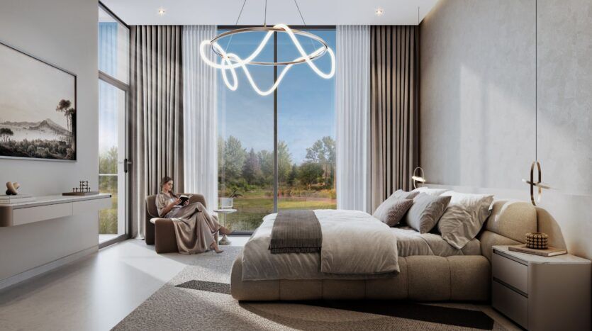 Une chambre à coucher moderne de The Terraces by Sobha se caractérise par un grand lit, des tons neutres et des fenêtres allant du sol au plafond. Une femme lit près de la fenêtre, sous un lustre circulaire unique, avec les arbres et le ciel visibles à l'extérieur.