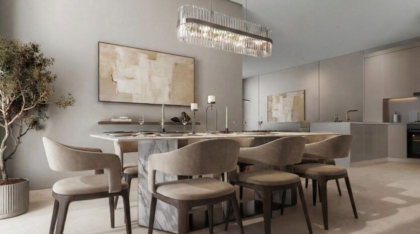 La salle à manger moderne de The Terraces by Sobha comprend une table rectangulaire pour six personnes, des chaises beiges rembourrées, un grand tableau abstrait, un lustre géométrique et une plante en pot, le tout dans des tons neutres et un décor minimaliste.