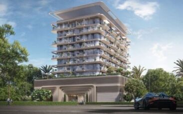Un bâtiment moderne de plusieurs étages avec de grands balcons et de la verdure est entouré d'arbres et de palmiers. Au premier plan, une voiture de sport élégante est garée sous un ciel bleu clair, reflétant le luxe de The Tides by Amis.