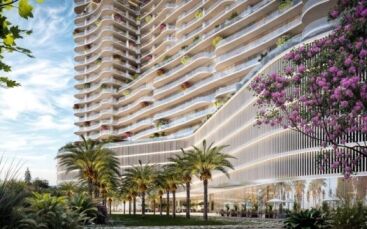 La Wow Tower est une tour moderne avec des balcons incurvés, une végétation luxuriante et des plantes à fleurs. Des palmiers et des jardins paysagers entourent sa base, avec de grandes fenêtres et des sièges extérieurs sous un ciel bleu parsemé de nuages.