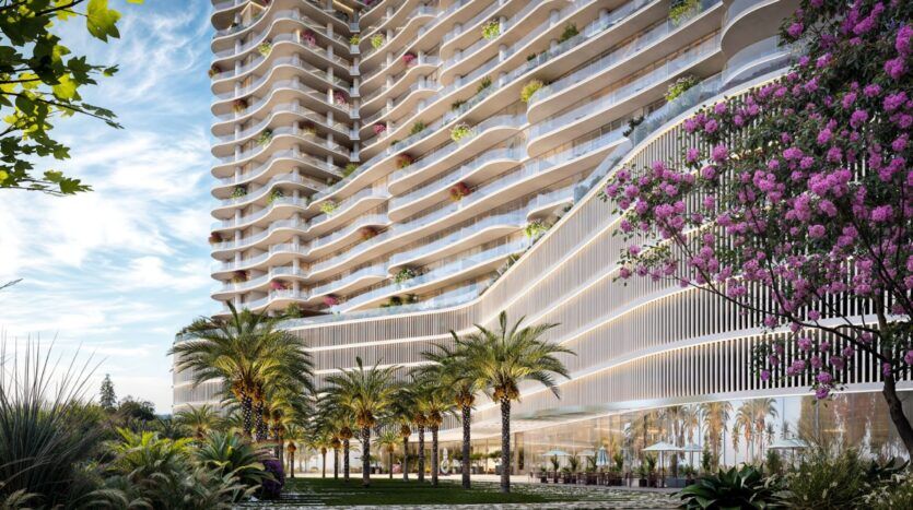 The Wow Tower is a modern tower featuring curved balconies, lush greenery, and flowering plants. Palm trees and landscaped gardens surround its base, with large windows and outdoor seating under a blue sky dotted with clouds.