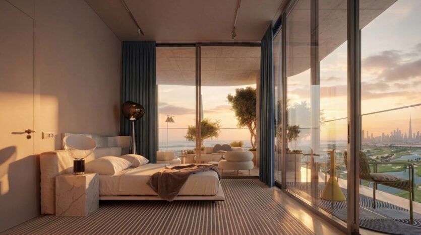 This modern room at the Wow Tower features floor-to-ceiling windows that open onto a balcony offering breathtaking views of the city at sunset. The room includes a bed, comfortable seating, and minimalist decor in neutral tones.