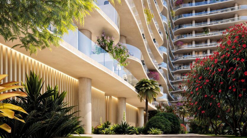 The contemporary apartment building, The Wow Tower, features curved balconies and glass railings. Surrounded by lush greenery and vibrant flowers, the inviting outdoor spaces are bathed in sunlight, creating a truly stunning atmosphere.