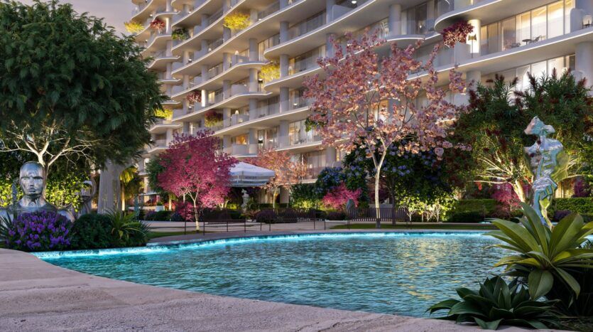 A pool surrounded by lush trees, colorful flowering plants, and statues sits in front of the modern Wow Tower apartment building, featuring curved balconies and lush greenery. Soft lighting creates a peaceful and welcoming atmosphere.