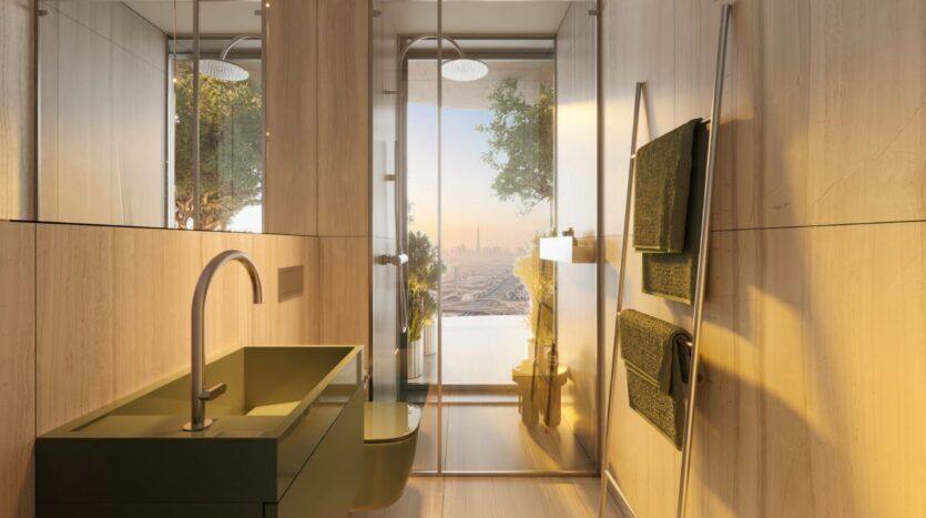 A modern bathroom with a green sink and toilet, light wood walls, a towel rack with green towels, and a large window overlooking the Wow Tower at sunset. The shower is equipped with a rain showerhead and offers a view of the tree outside.