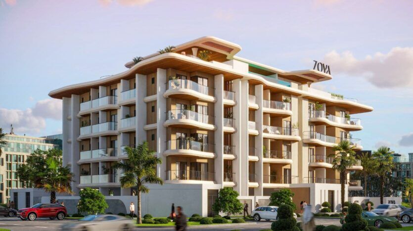 Un immeuble d'appartements moderne de plusieurs étages - Calisi by Zoya - avec des balcons incurvés, de grandes fenêtres et des palmiers. Plusieurs voitures et personnes longent la rue en contrebas, avec l'enseigne "ZOYA" bien en évidence sur le toit.