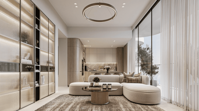 Un salon moderne avec un canapé blanc incurvé, une table basse ronde et des étagères ouvertes doucement éclairées. De grandes fenêtres allant du sol au plafond avec des rideaux transparents inondent l'espace de lumière. Le coin cuisine et l'œuvre d'art Cybele by Wadan sont visibles à l'arrière-plan.