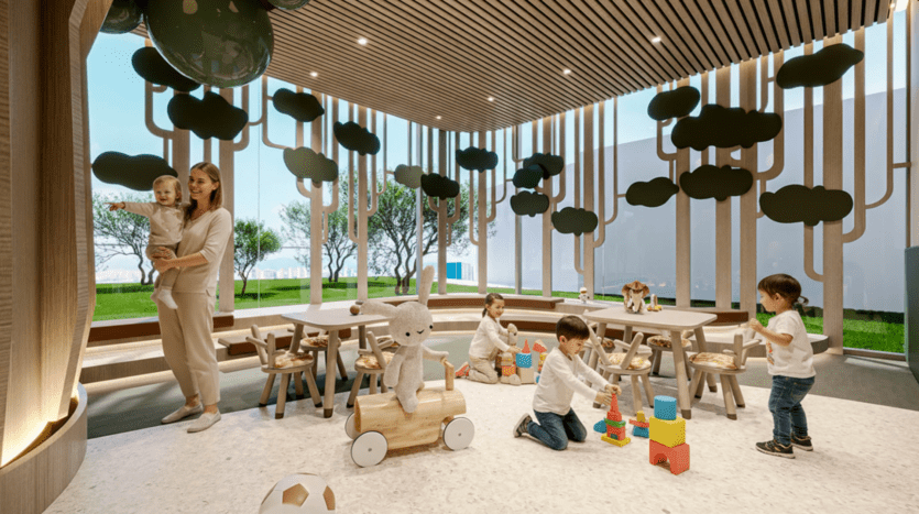 Une salle de jeux moderne et lumineuse présente un décor en bois en forme d'arbre, plusieurs enfants s'amusant avec des jouets et des blocs, et un adulte tenant un jeune enfant dans ses bras. De grandes fenêtres éclairent l'espace, tandis que le mobilier Cybele by Wadan apporte une touche de charme.