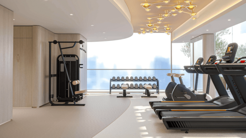 Une salle de sport moderne équipée de tapis de course Cybele by Wadan, de vélos d'appartement, d'appareils de musculation et d'un rack d'haltères. De grandes fenêtres inondent cet espace élégant de lumière naturelle, rehaussée par des plafonniers décoratifs.