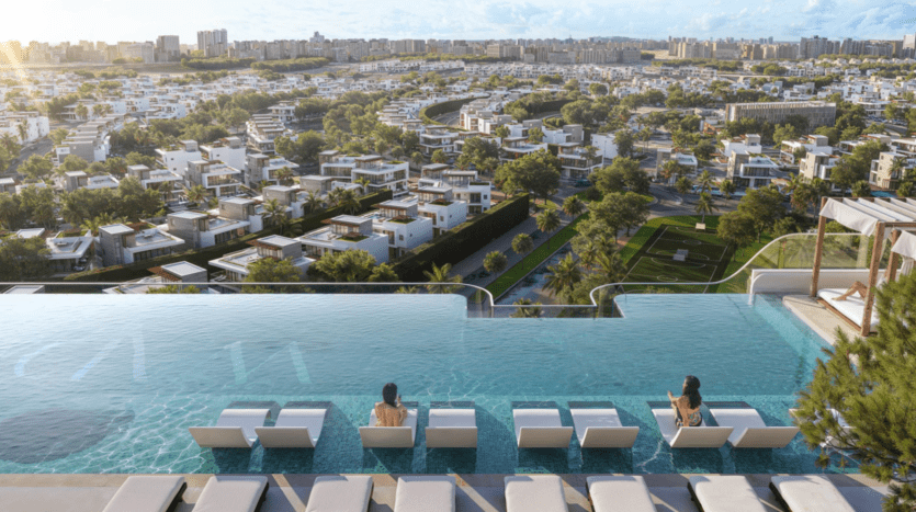 La piscine à débordement sur le toit du Cybele by Wadan, où des personnes se prélassent, surplombe un paysage urbain tentaculaire de villas blanches modernes et de verdure luxuriante sous un ciel bleu.