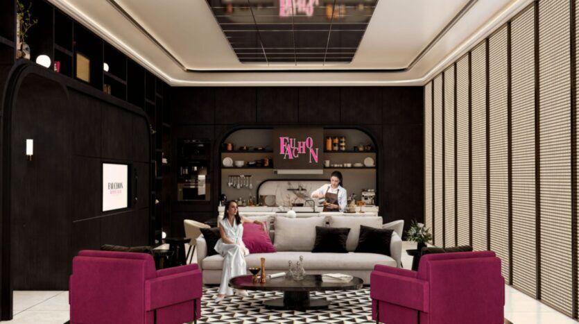 Un salon moderne de la résidence Fauchon présente des murs sombres, des fauteuils roses, un canapé blanc et un tapis géométrique. Une femme se détend sur le canapé tandis qu'un homme prépare des boissons dans un petit bar sous un néon "FASHION".