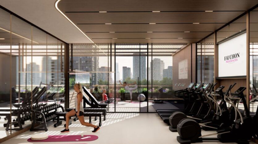 Salle de sport moderne de la résidence Fauchon, avec de grandes fenêtres donnant sur l'horizon de la ville, équipée de tapis de course, de poids, de miroirs et de tapis d'exercice. Une personne fait des fentes tandis qu'une autre s'étire près de la fenêtre.