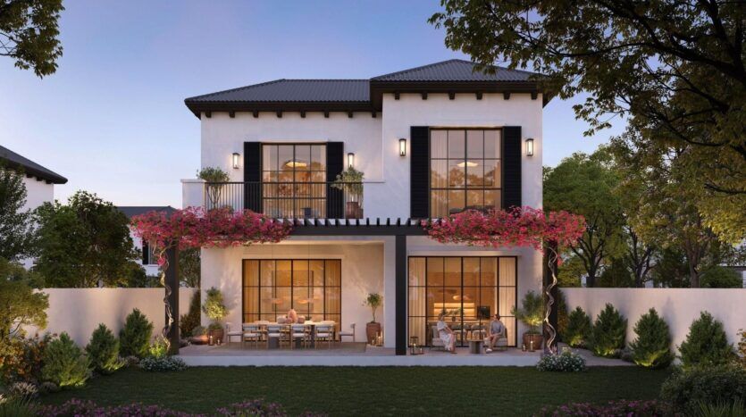 Maison moderne de deux étages avec de grandes fenêtres, un balcon et un patio à Hudayriyat Golf Estates. Des vignes à fleurs roses grimpent le long des pergolas. Des sièges extérieurs sont disposés au rez-de-chaussée, entourés d'arbustes, d'arbres et d'une pelouse verte.