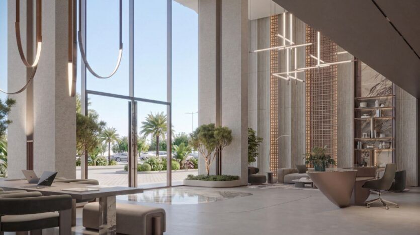 Le hall moderne de l'Oxford Cove by Iman présente de hauts plafonds, des fenêtres allant du sol au plafond, des luminaires contemporains, un mobilier épuré, des arbres d'intérieur et offre une vue lumineuse sur les palmiers et les voitures à l'extérieur.