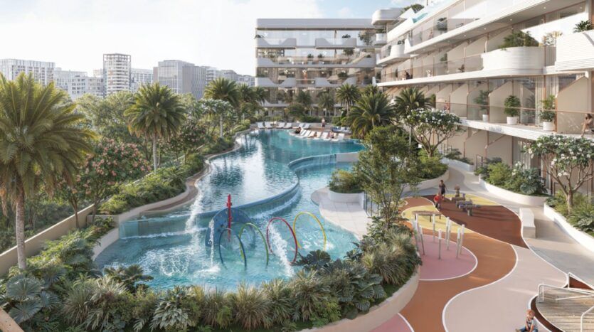 Oxford Cove by Iman est un hôtel moderne ou un complexe d'appartements avec des balcons incurvés, donnant sur une piscine de style balnéaire avec des jeux d'eau, entourée de palmiers, de chaises longues et de verdure luxuriante dans un cadre urbain ensoleillé.