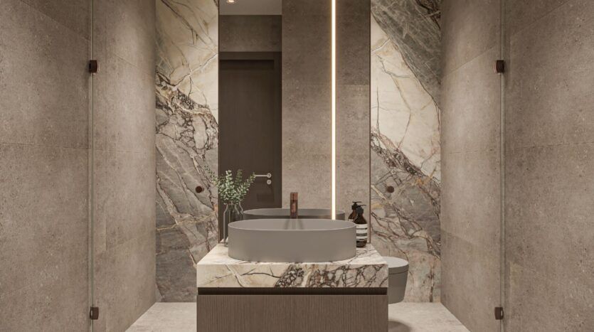 Salle de bains moderne avec des murs en pierre beige, un grand accent en marbre derrière le lavabo, une vasque ronde grise sur un meuble-lavabo en marbre, et un éclairage vertical doux par un grand miroir - élégamment stylé avec Oxford Cove d'Iman.