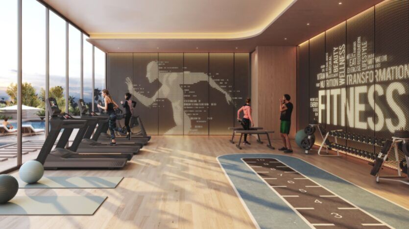 Salle de sport spacieuse des résidences Rotana, avec de grandes fenêtres, des tapis roulants et des équipements d'exercice. Une fresque murale présente des mots sur le thème du fitness et un personnage en train de courir. À l'extérieur, une piscine et des chaises longues sont visibles.