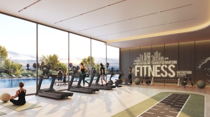 Une salle de sport moderne dans les résidences Rotana avec de grandes fenêtres donnant sur une piscine, avec des tapis de course, des personnes faisant de l'exercice, des tapis de yoga, des équipements de fitness et un mur avec des mots motivants comme "FITNESS" et "TRANSFORMATION".
