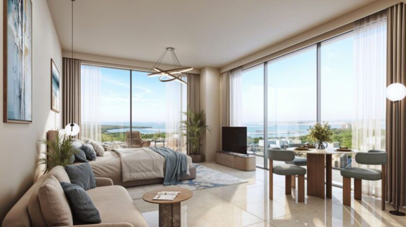 Cet appartement moderne et ensoleillé de Rotana Residences comprend un lit, un canapé, une petite table à manger et de grandes fenêtres offrant une vue pittoresque sur la mer et la verdure. Les tons neutres et la décoration contemporaine créent une atmosphère aérée et accueillante.