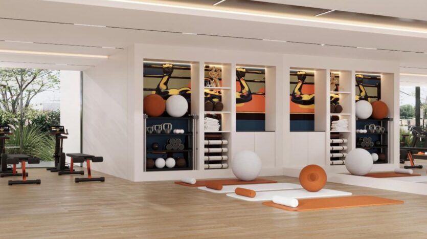 Salle de sport moderne de Winslow avec des sols en bois, des tapis d'exercice, des bancs, des poids et des étagères contenant des ballons de yoga, des serviettes et de l'équipement. De grandes fenêtres inondent l'espace de lumière naturelle, tandis que des œuvres d'art murales colorées décorent le mur du fond.