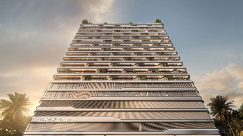 Un immeuble moderne de grande hauteur, aux lignes horizontales épurées, avec des balcons en verre et de la verdure sur plusieurs niveaux, s'élève au-dessus. L'enseigne indique "Tresora by Wadan", tandis que des palmiers encadrent élégamment l'impressionnante structure.