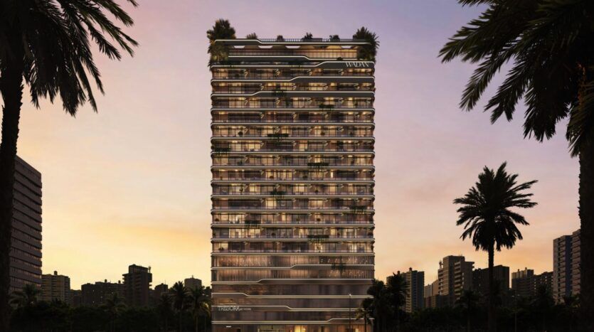Une tour moderne, Tresora par Wadan, présente des balcons illuminés et de la verdure sur plusieurs étages dans un ciel de coucher de soleil. Des palmiers encadrent la scène, tandis que les bâtiments de la ville sont visibles en arrière-plan.