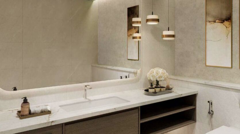 Salle de bains moderne avec un comptoir en marbre, un lavabo, un distributeur de savon, des serviettes et un plateau avec des fleurs décoratives. Les lampes suspendues et l'art mural abstrait au-dessus du meuble-lavabo créent un look luxueux inspiré par Arancia Yards by Beyond. Un grand miroir reflète l'élégance du décor.