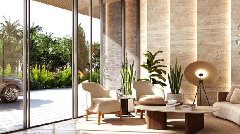 Hall d'entrée moderne à Arancia Yards by Beyond avec de grandes fenêtres, des fauteuils beiges, des tables en bois, des plantes d'intérieur et un lampadaire. La lumière du soleil pénètre à flots, mettant en valeur les murs texturés, la verdure et une voiture garée à l'extérieur.