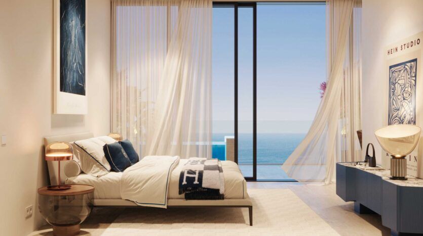 La chambre à coucher moderne de la Villa del Garda est dotée d'une grande porte vitrée donnant sur l'océan. Des rideaux diaphanes flottant au gré de la brise, un éclairage doux, un lit double aux accents bleus et une décoration contemporaine créent une atmosphère sereine et aérée.