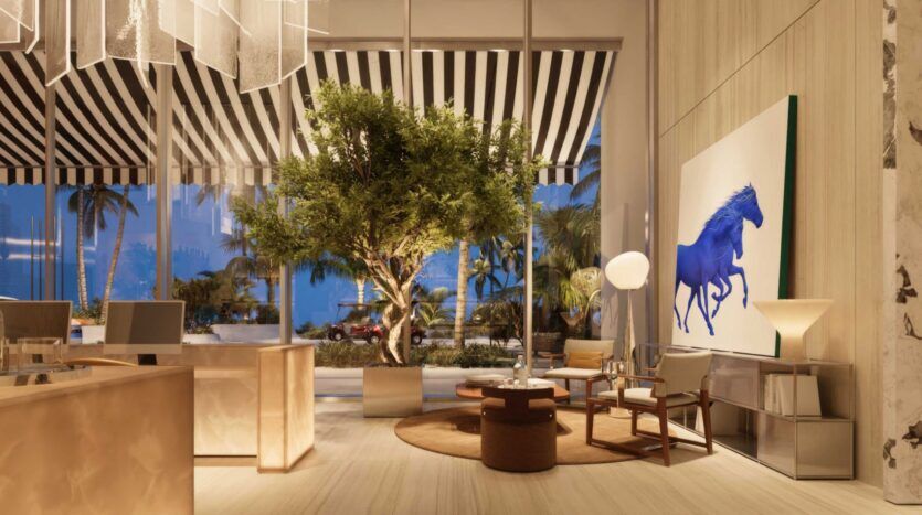 Le hall moderne et élégant de la Villa Del Garda est doté de grandes fenêtres, d'un auvent rayé, d'un arbre en pot, d'un mobilier contemporain et d'une œuvre d'art représentant un cheval bleu. Des palmiers et une voiture sont visibles à l'extérieur au crépuscule.