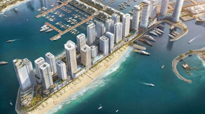 Vue aérienne d'un développement urbain côtier avec des gratte-ciel près d'une marina remplie de bateaux, à côté d'une plage de sable aux eaux turquoise claires.