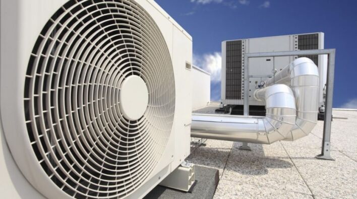 Une grande unité de climatisation industrielle dotée d'un ventilateur circulaire proéminent, positionnée sur le toit d'un immeuble à Dubaï sous un ciel bleu clair.