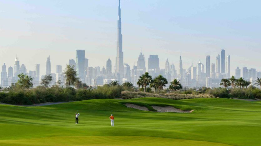 Deux golfeurs sur un parcours vert vif avec un bunker de sable, mettant en avant une vue panoramique sur les toits de Dubaï, y compris le Burj Khalifa, situé dans l'un des meilleurs quartiers de Dubaï.