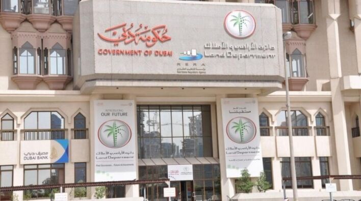 Façade d'un bâtiment gouvernemental à Dubaï, affichant des panneaux indiquant le Département foncier de Dubaï et le RERA, avec un panneau Immobilier Dubaï en dessous. L'architecture est moderne avec des éléments traditionnels.