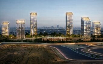 Six gratte-ciel modernes en verre du quartier O1NE, illuminés à la tombée de la nuit, se dressent au milieu de la verdure, avec la silhouette de la ville en arrière-plan et des routes sinueuses au premier plan.
