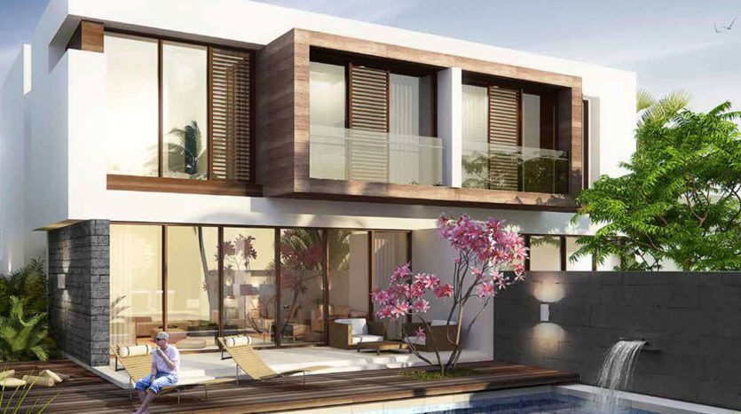 Une maison moderne de deux étages à Damac Hills avec de grandes fenêtres et des touches de bois, entourée d'une verdure luxuriante. Un arbre à fleurs roses fleurit au bord d’une piscine avec une personne se relaxant sur une chaise longue.